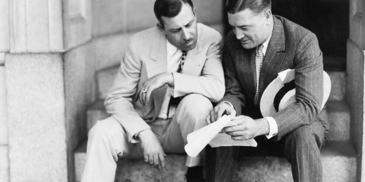 Two men sitting on steps and reading a document
